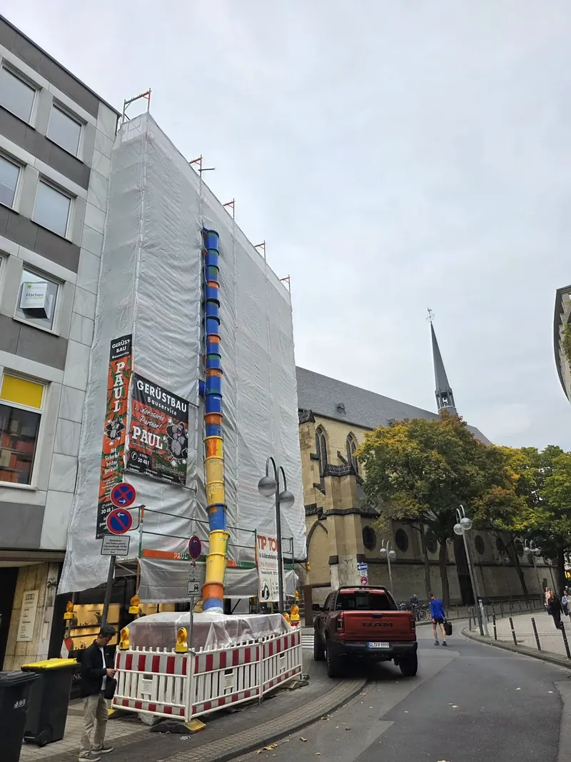 Vollflächig mit Planen eingehaustes Eckgebäude am Kolpingplatz mit Bauschuttrutsche und Paul-Gerüstbau-Banner